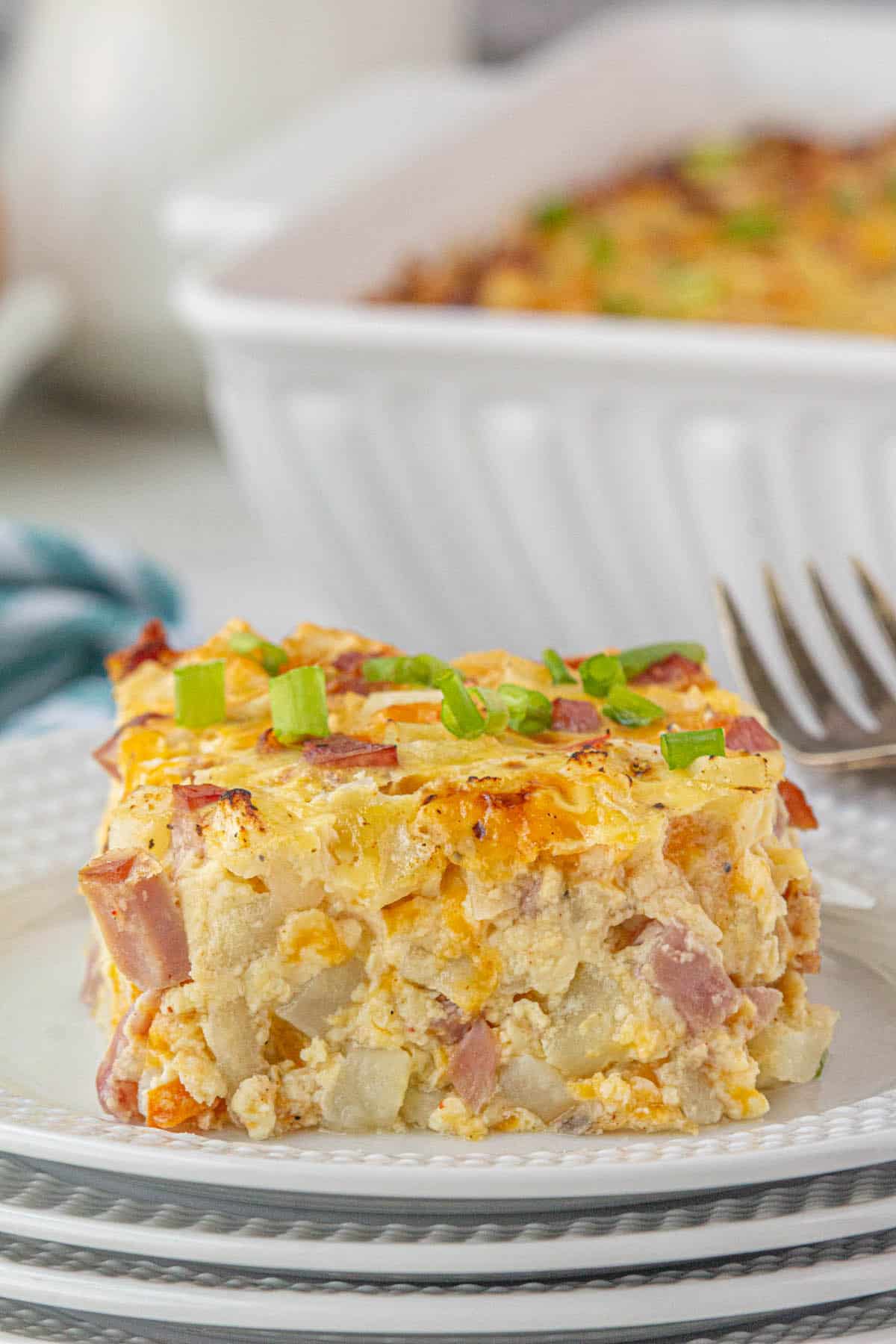 A slice of Ham and Egg Hashbrown Casserole on a plate, with a fork in the background.