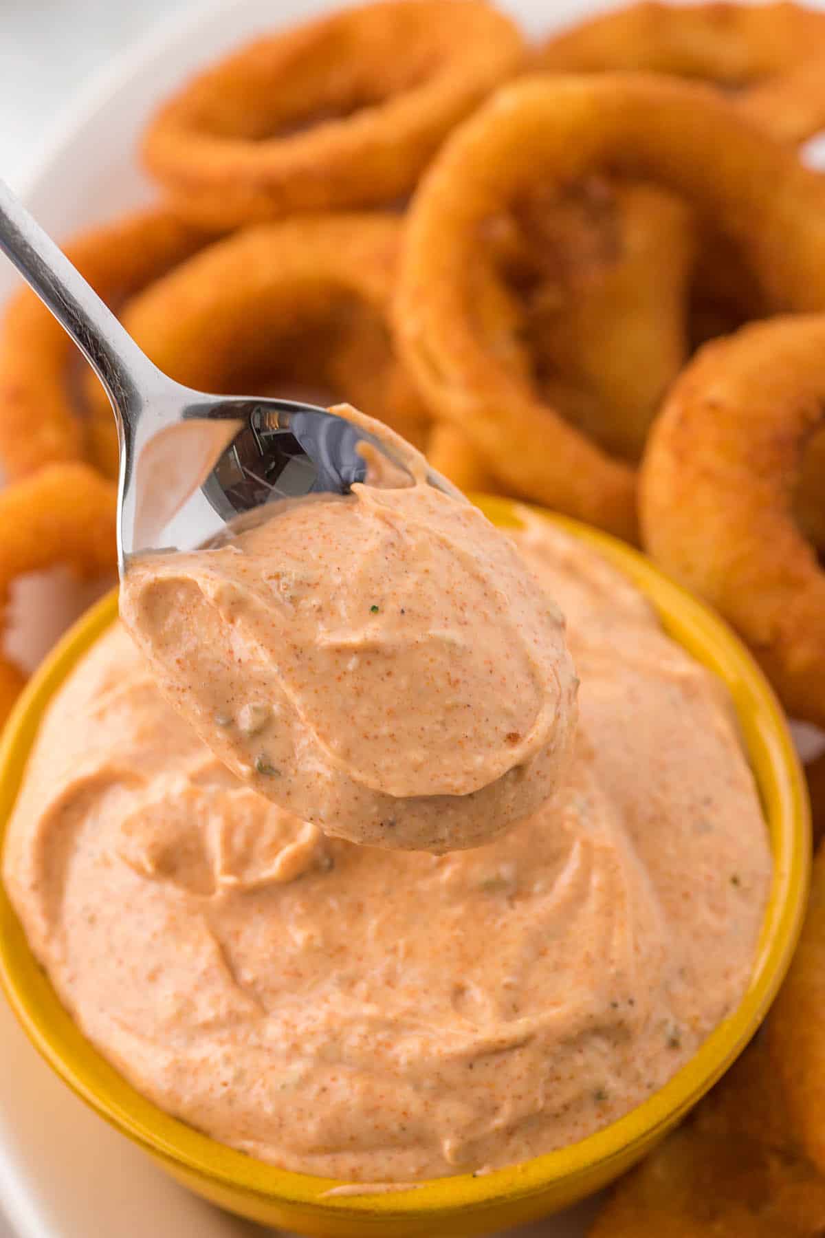 A yellow bowl filled with copycat Outback blooming onion sauce. With a spoon taking a scoop of the sauce.