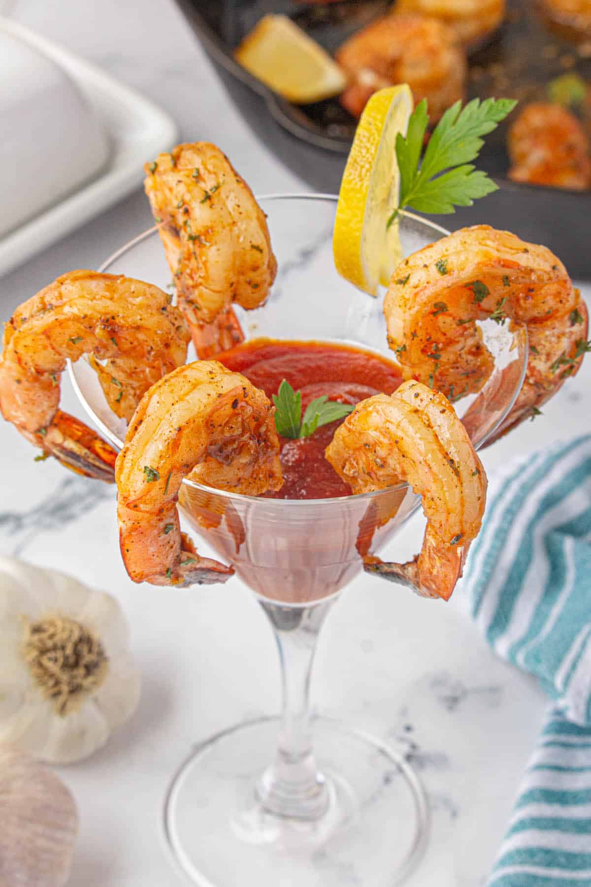 A martini glass filled with red cocktail sauce. There are a ring of fried shrimp hooked around the edges, with a wedge of lemon.