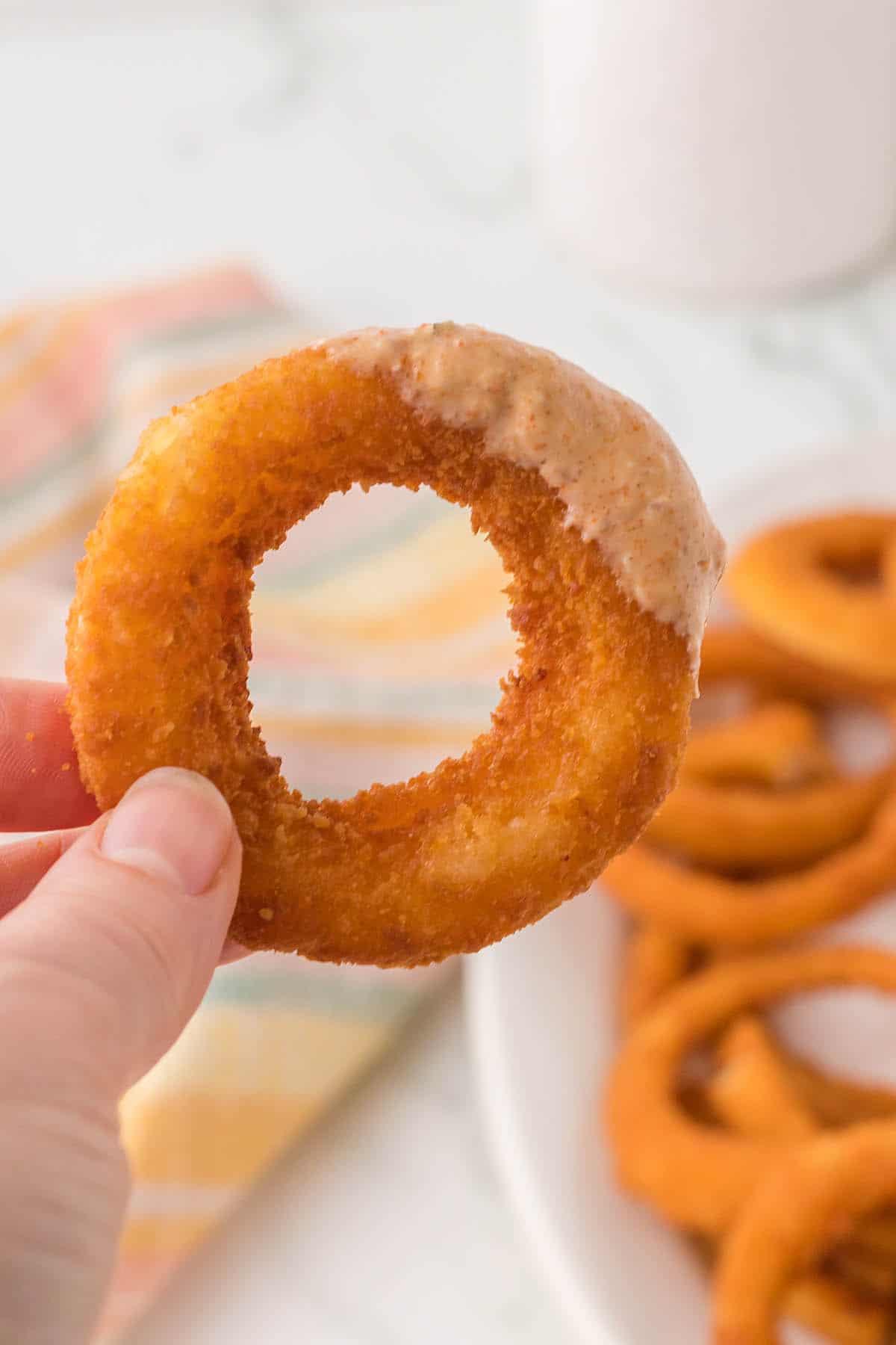 A hand holding a crispy onion ring that was dipped in sauce.