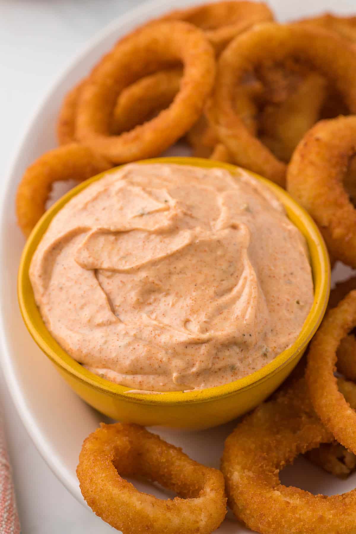 A bowl filled with blooming onion sauce surrounded by onion rings on a white platter.