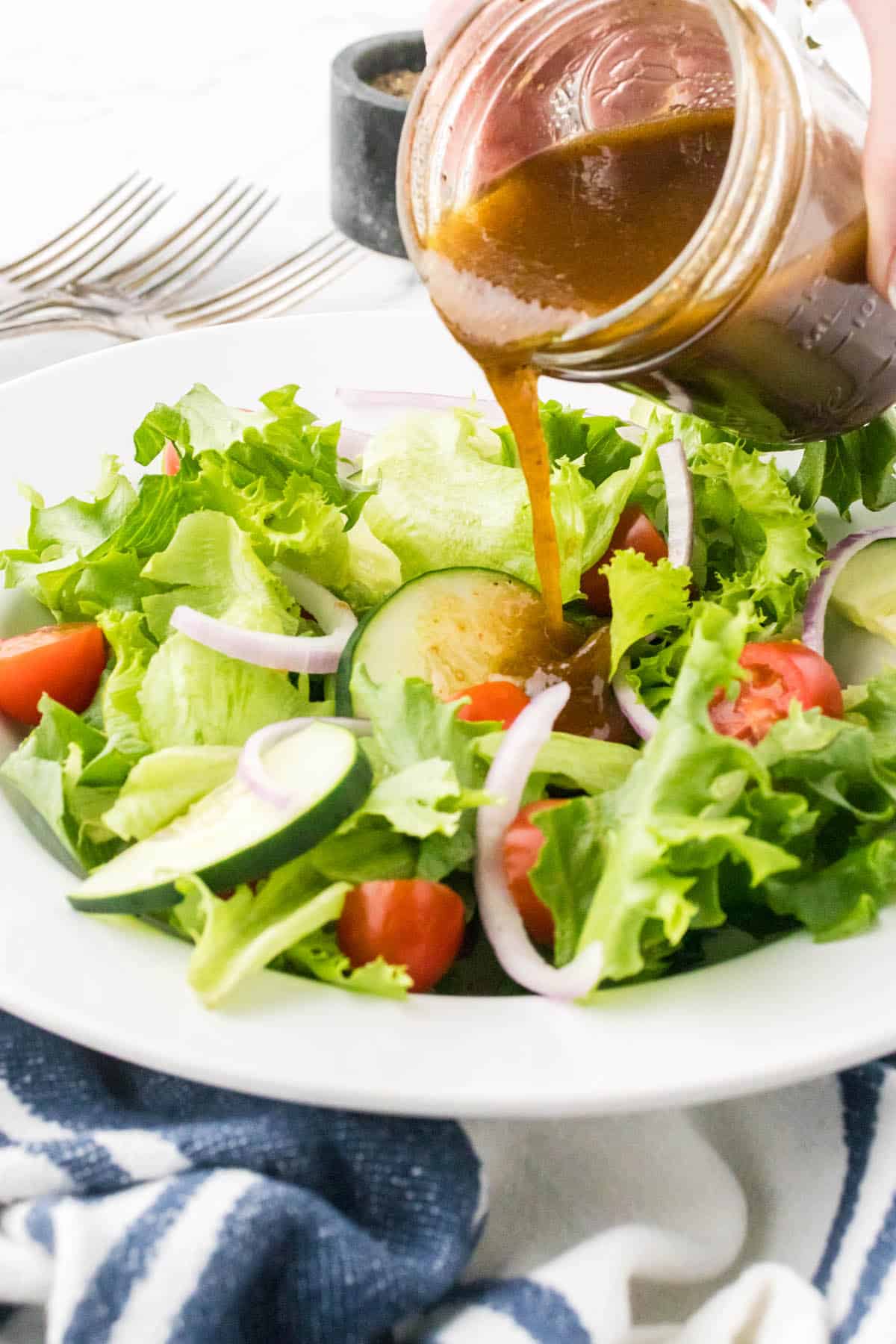 A green salad in a bowl, with balsamic vinaigrette being drizzled over the salad.