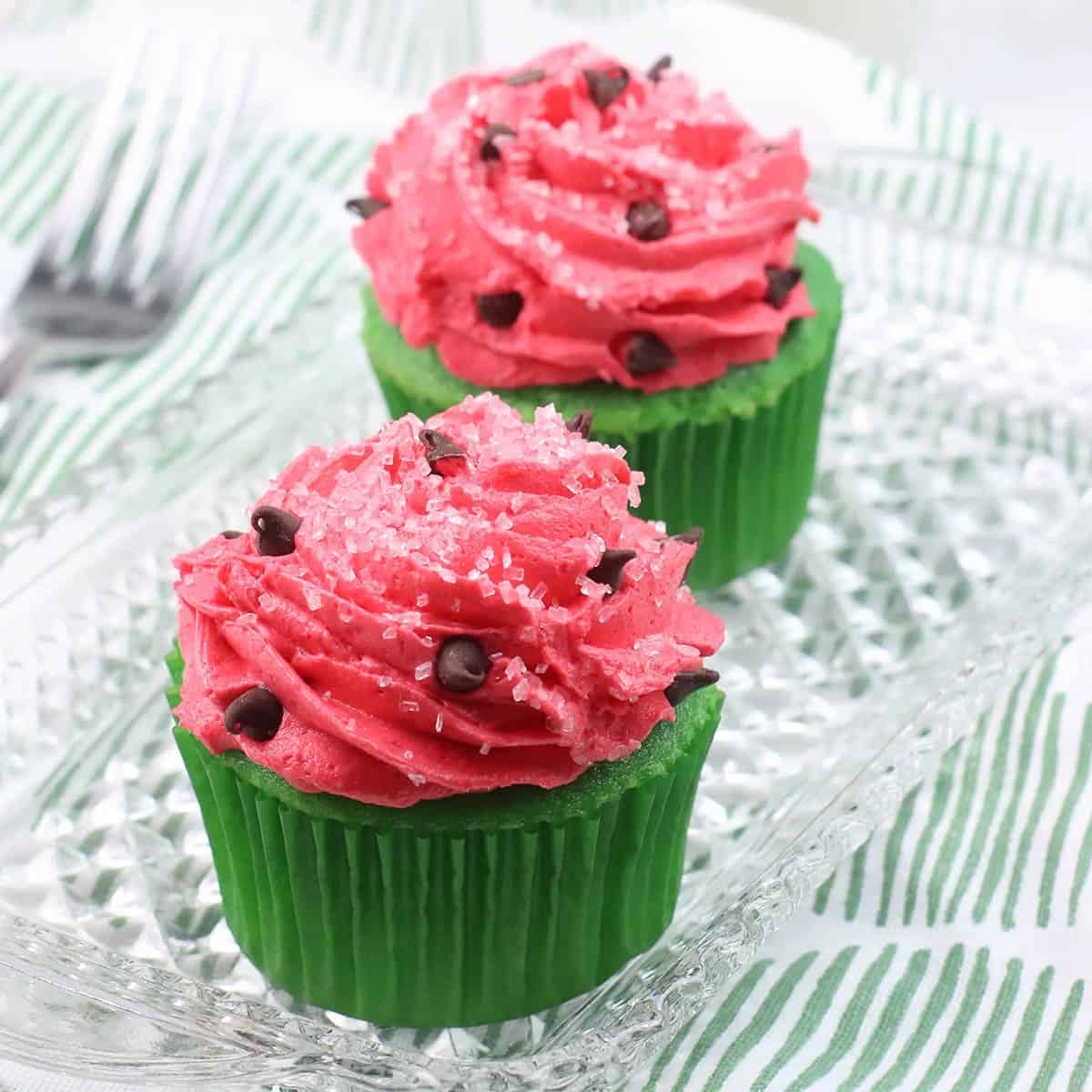 Two watermelon cupcakes on a pretty glass platter.