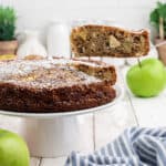 Sliced apple tea cake on a cake plate. A spatula is serving up a slice.