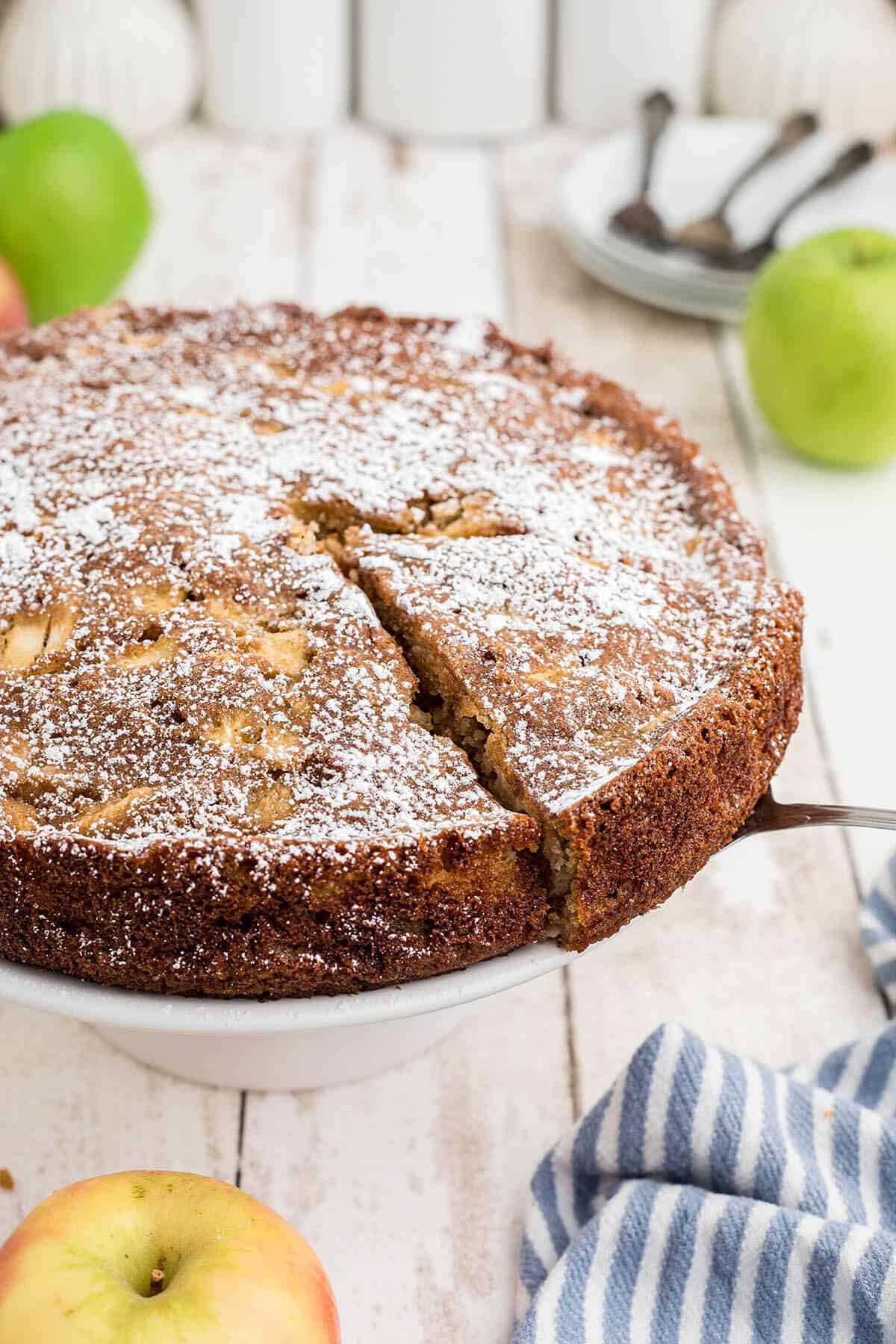 Apple Tea Cake on a cake plate. There's a serving spatula removing a slice of cake.