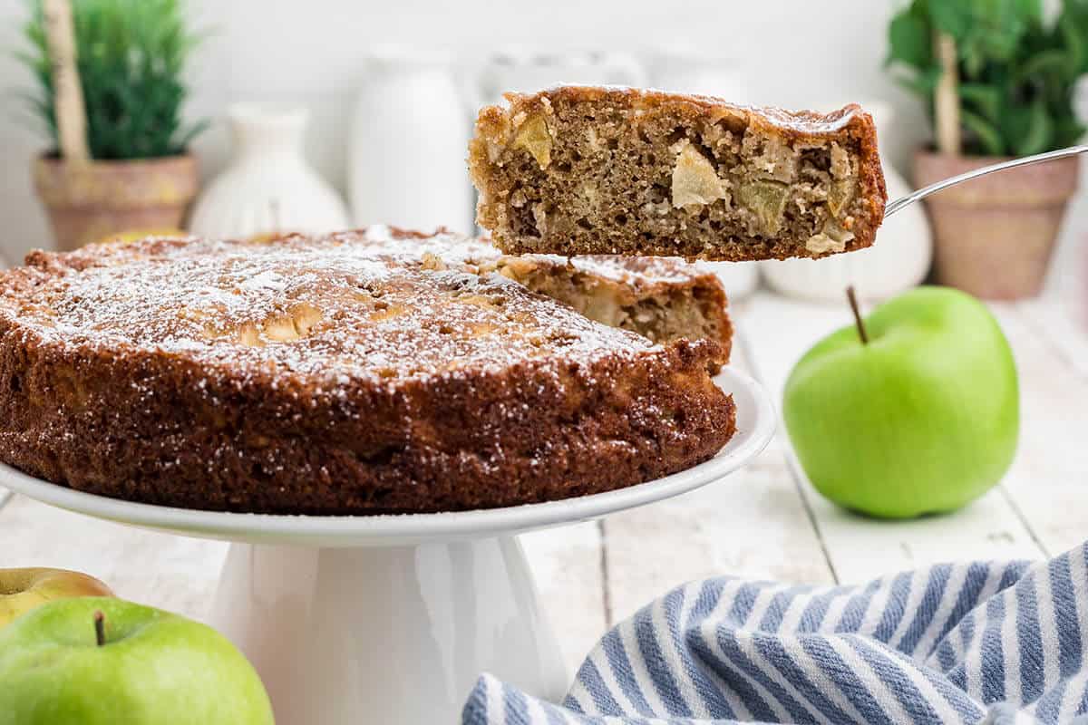 Apple Tea Cake on a cake plate. A spatula is removing a slice.