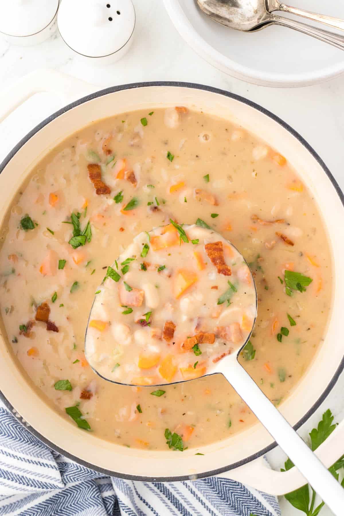 A big pot filled with bean with bacon soup. A ladle is removing a big scoop of soup.