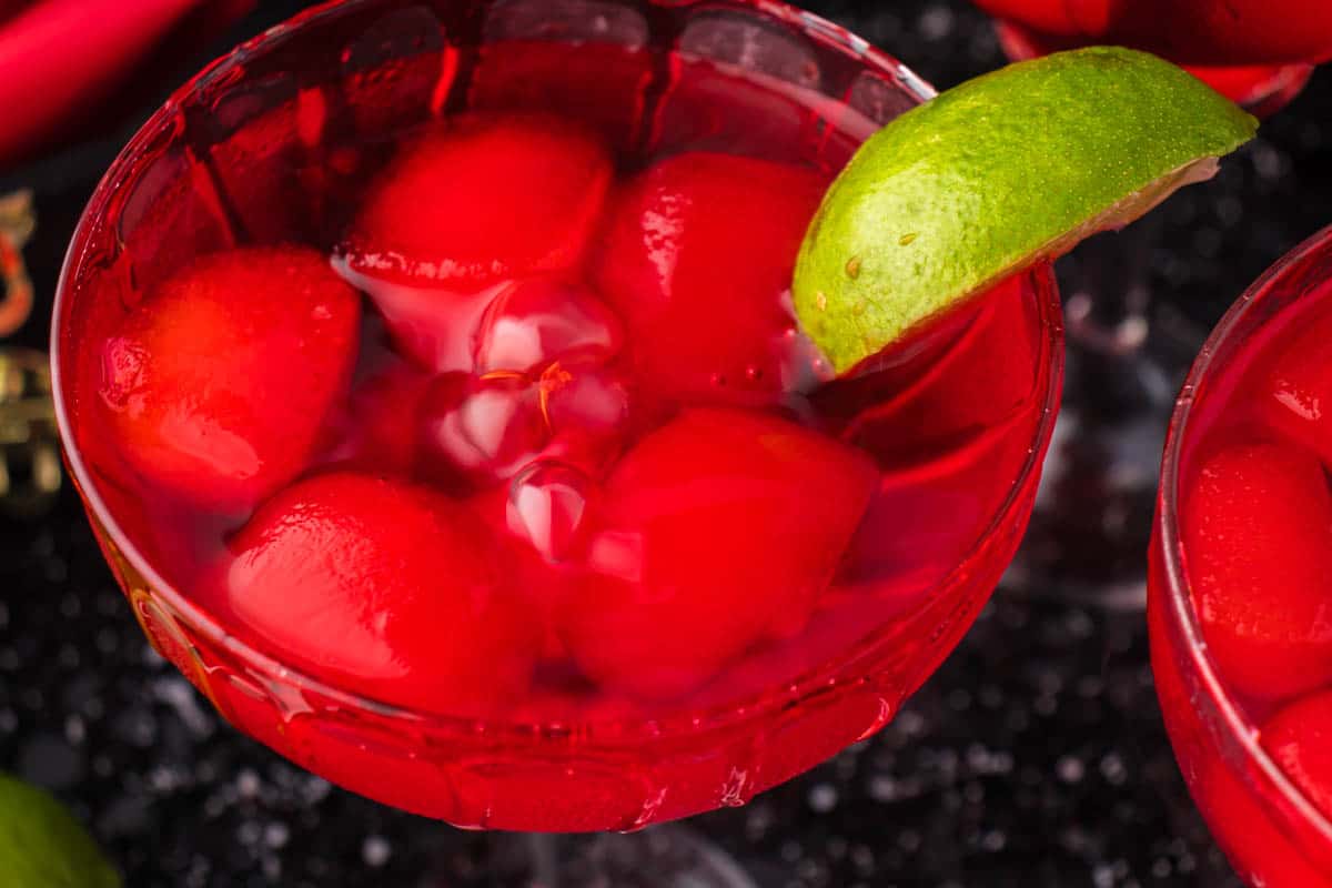 A blood margarita in a cocktail glass garnished with a slice of lime.