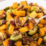 A large bowl filled with roasted butternut squash and brussels sprouts. With a serving spoon.