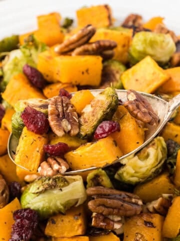 A large bowl filled with roasted butternut squash and brussels sprouts. With a serving spoon.