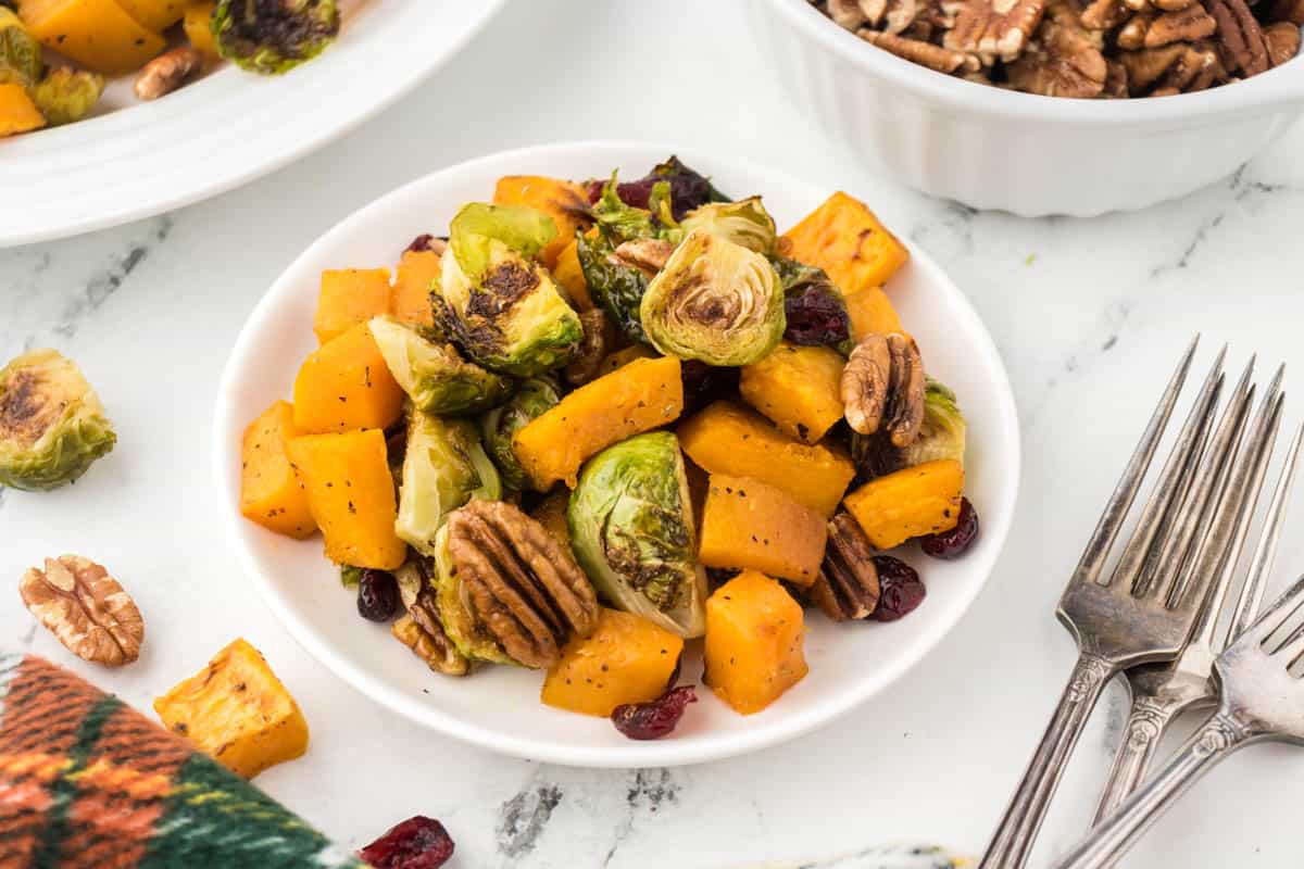 A small bowl filled with roasted brussels sprouts and butternut squash. With forks on the side.