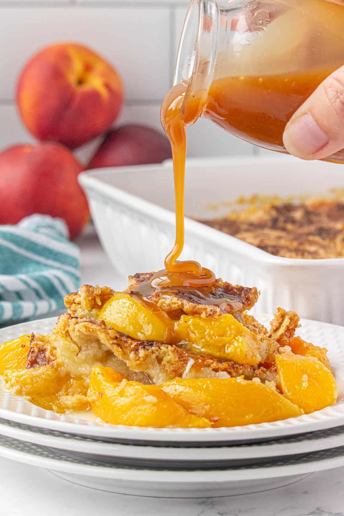 Peach cobbler on a plate. There's caramel sauce being drizzled over the cobbler.