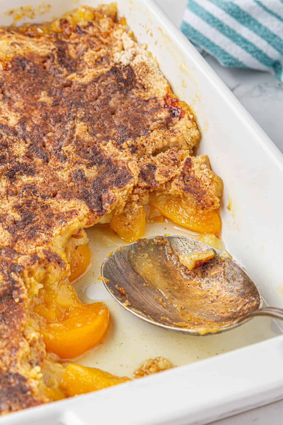 A baking dish filled with peach cobbler, with a spoon for dishing up the dessert.