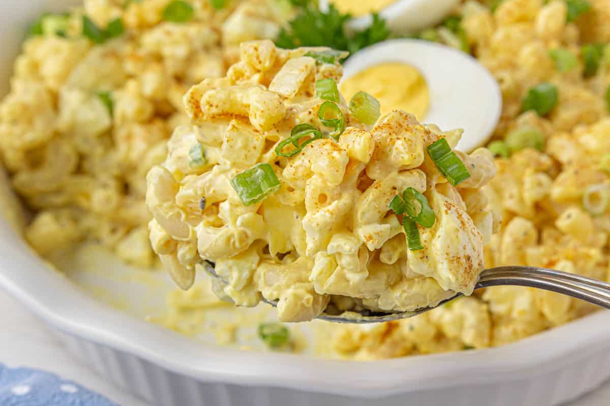 A large bowl filled with pasta salad with deviled eggs. With a serving spoon grabbing a scoop of salad.