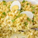 A serving spoon scooping out a big helping of deviled egg pasta salad from a bowl.