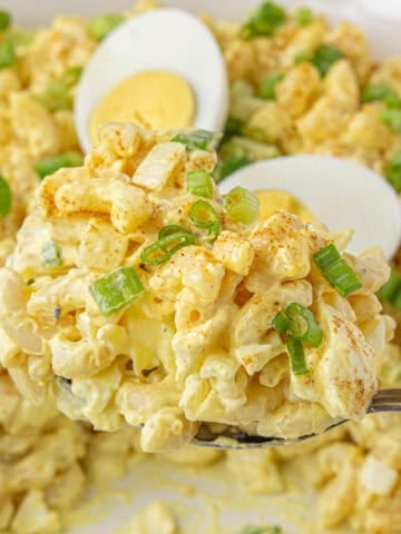 A serving spoon scooping out a big helping of deviled egg pasta salad from a bowl.