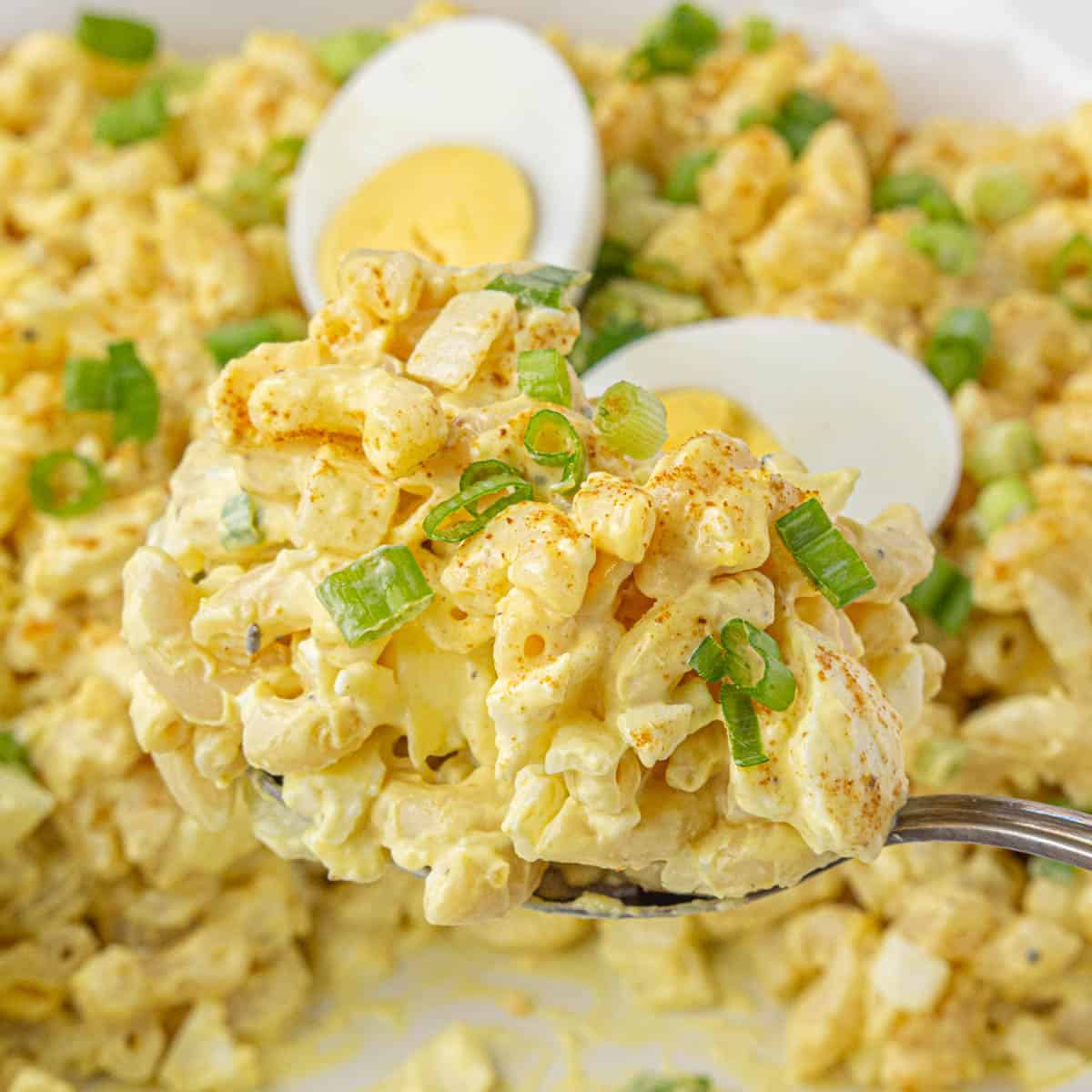 A serving spoon scooping out a big helping of deviled egg pasta salad from a bowl.