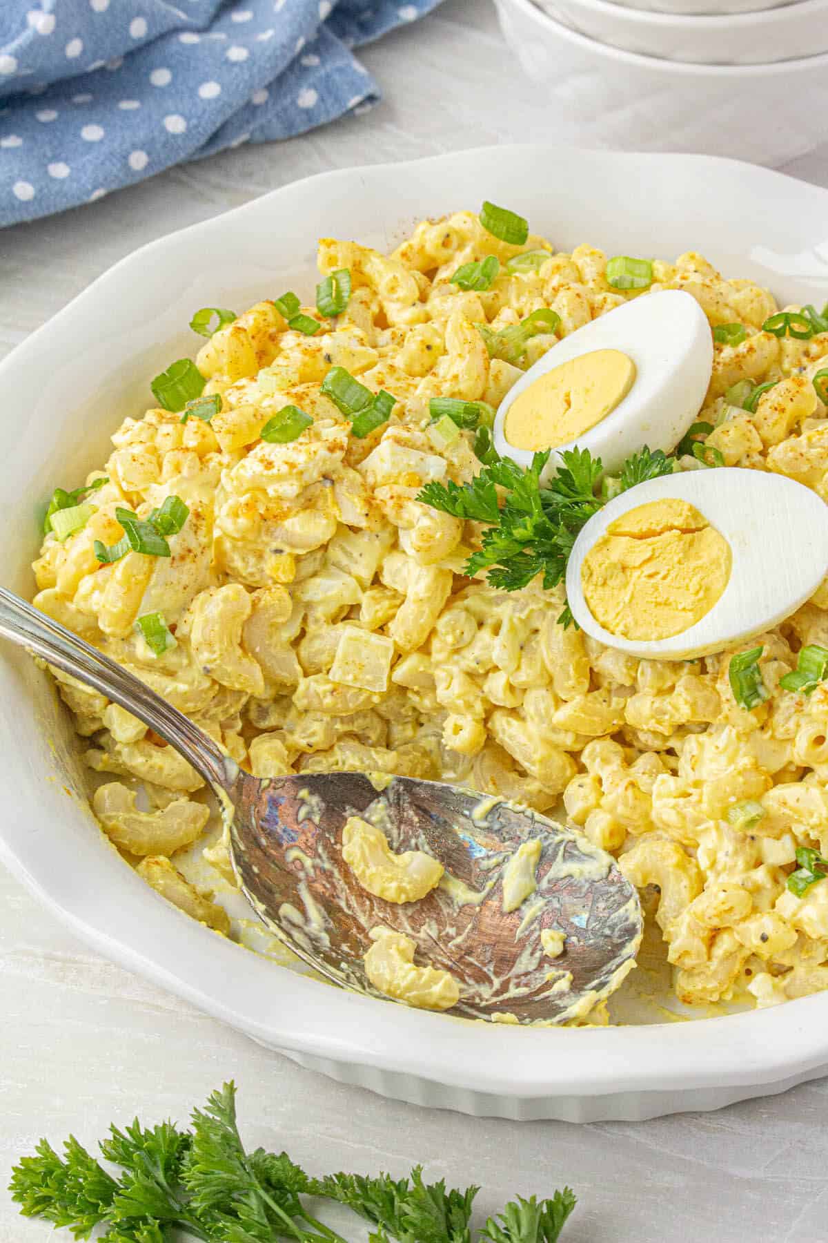 Deviled egg pasta salad in a large bowl, with a serving spoon ready to scoop out pasta.