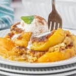 Peach cobbler topped with ice cream on a plate with a fork.