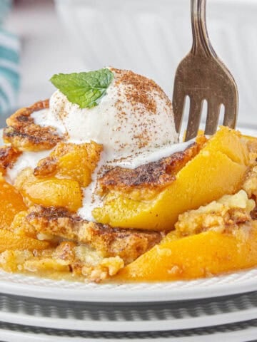 Peach cobbler topped with ice cream on a plate with a fork.