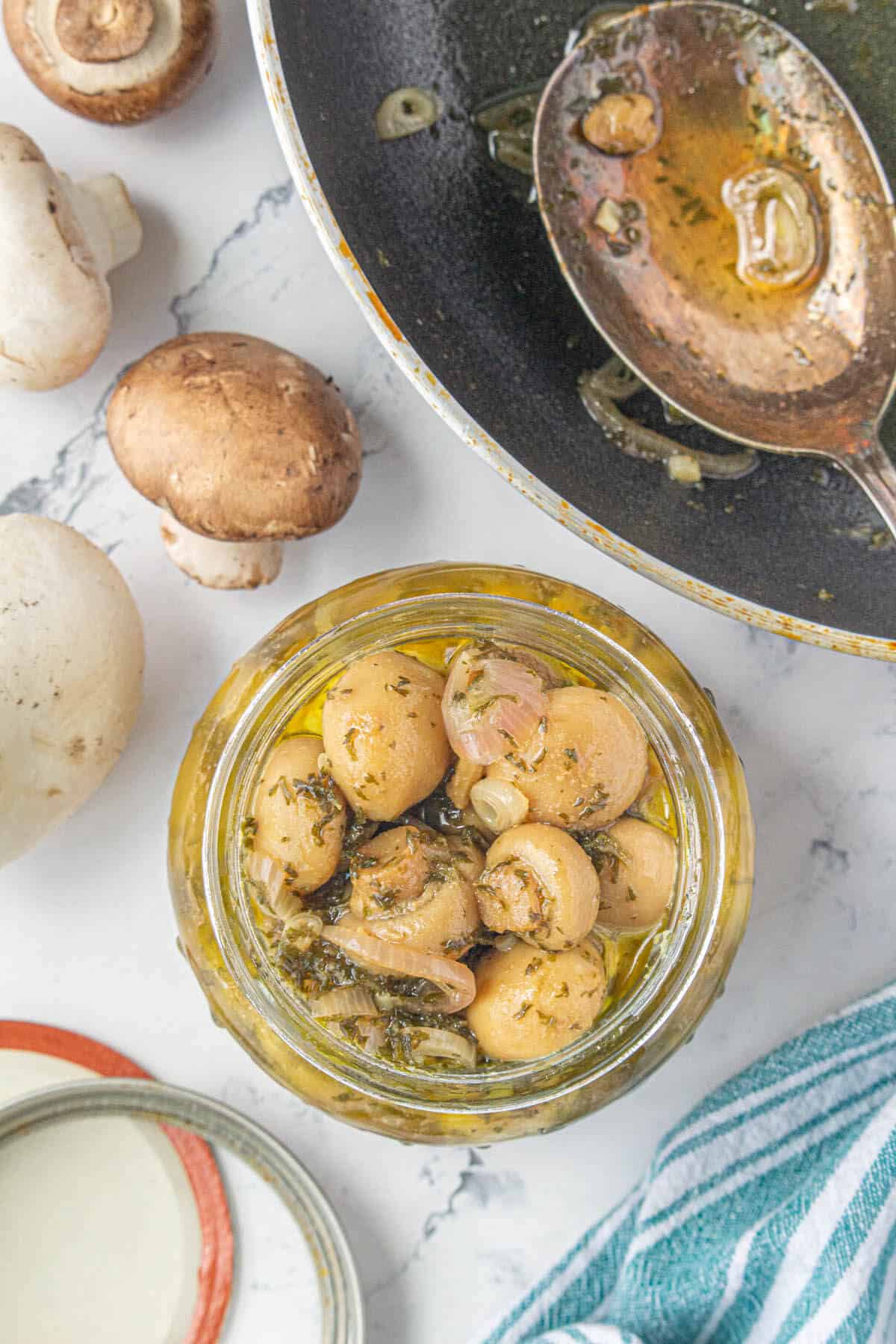 A jar of pickled mushrooms and shallots next to a fry pan.