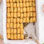 An overhead photo of ground beef tater tots in a casserole with a spatula for serving.