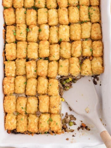 An overhead photo of ground beef tater tots in a casserole with a spatula for serving.