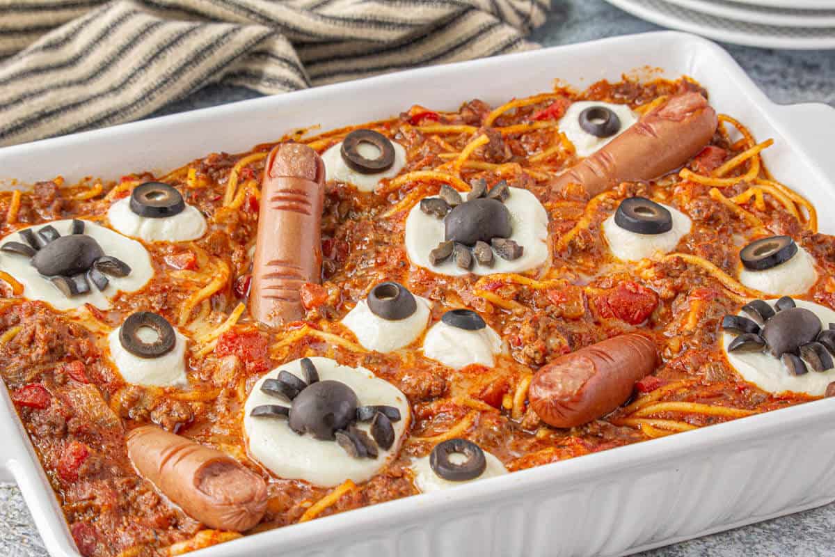 A casserole dish filled with a fun Halloween pasta recipe. Topped with cheesy eyes, hot dog fingers, and spiders is creepy and fun.