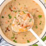 A soup pot filled with bean with bacon soup, with a ladle removing a scoop.