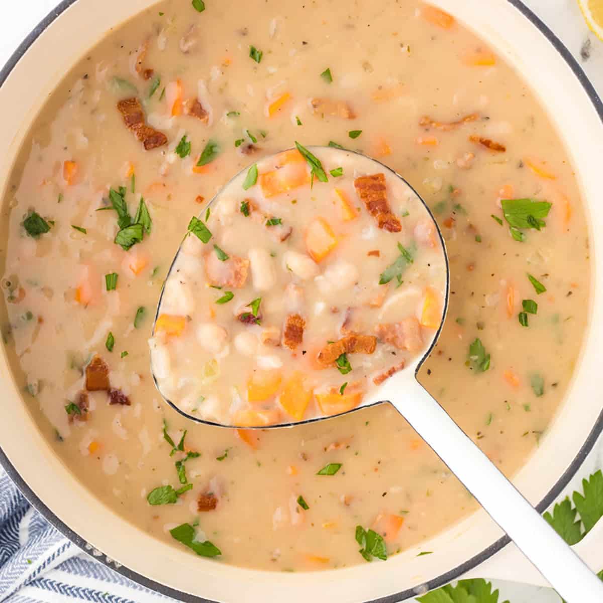 A soup pot filled with bean with bacon soup, with a ladle removing a scoop.