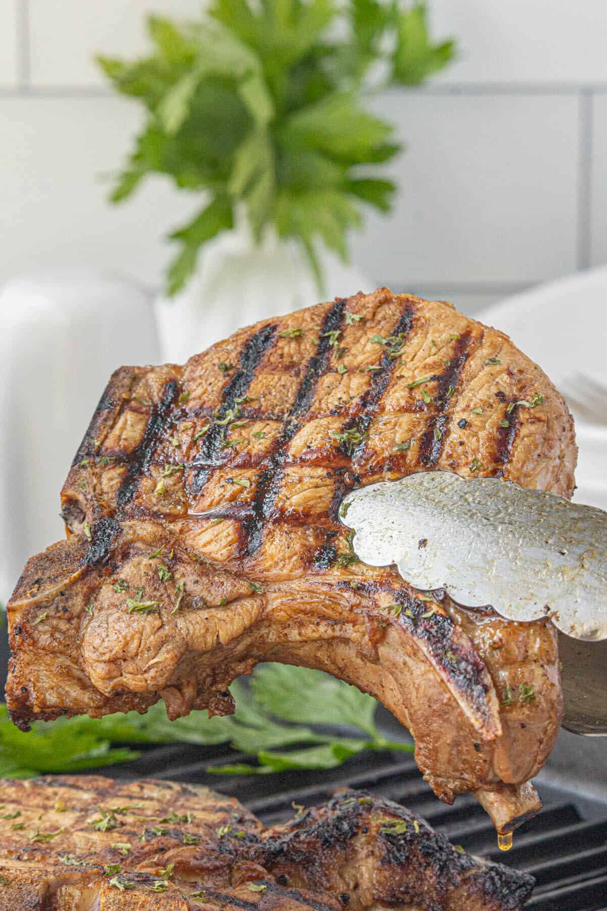 Texas Roadhouse grilled pork chops being held by thongs, taking it off the grill.