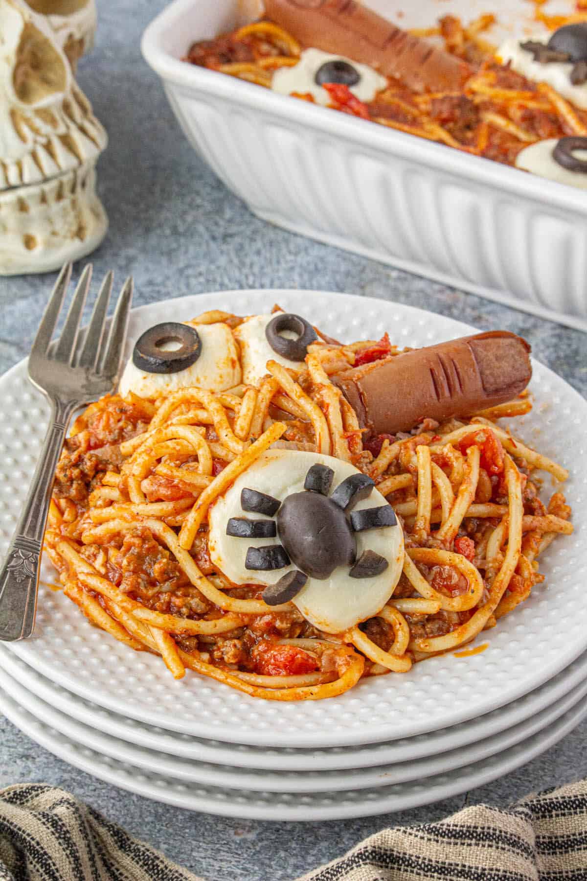 Creepy Halloween pasta on a plate. There are cheesy spiders made from olives, eyes and hot dog fingers on the plate.