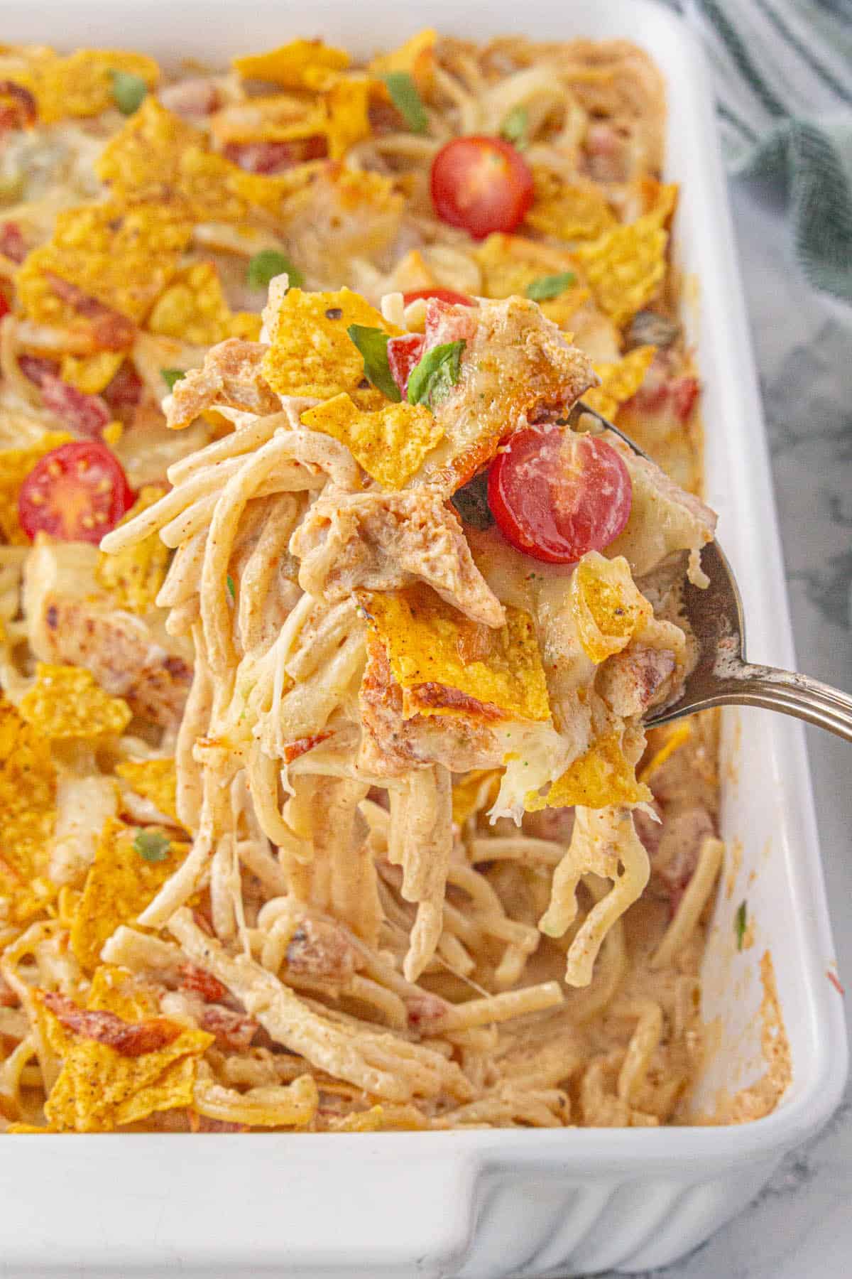 A serving spoon taking a scoop of queso chicken spaghetti from a casserole dish.