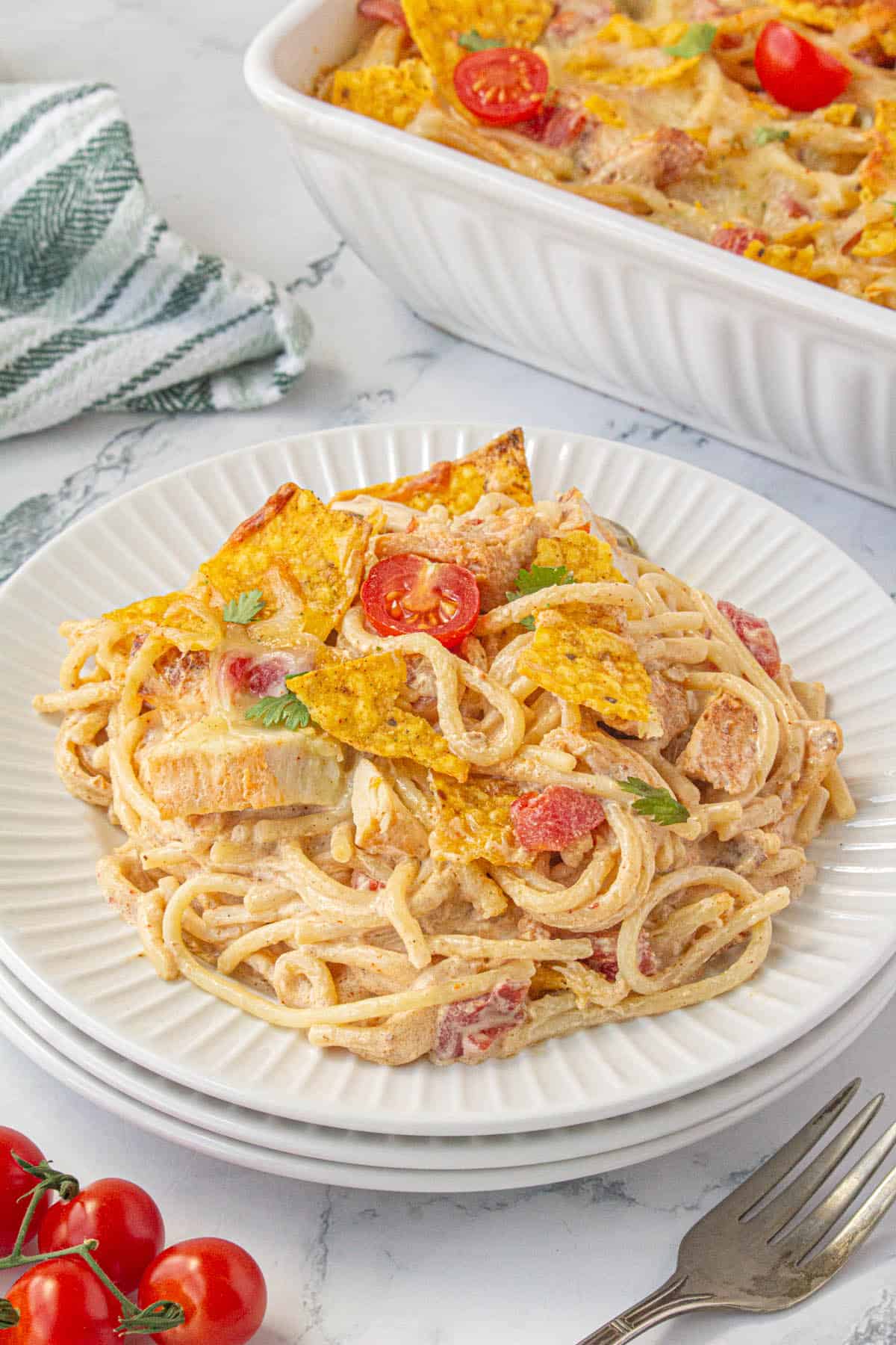 A plate piled high with Queso Chicken Spaghetti. The casserole is in the background.