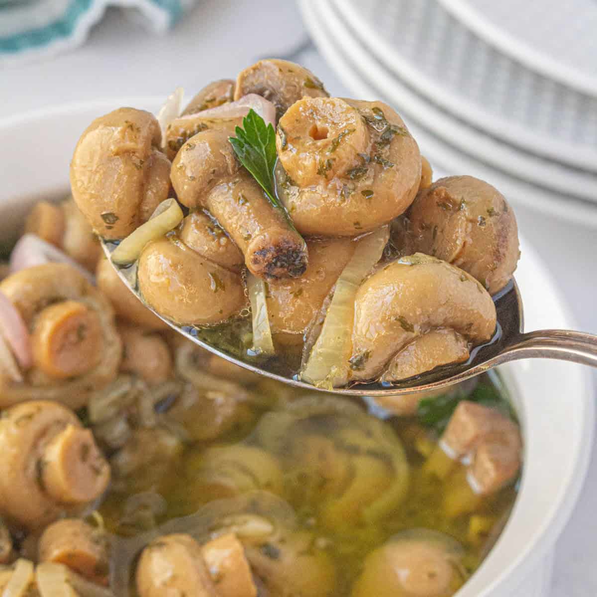 A spoon taking a scoop out of a bowl of pickled mushrooms.