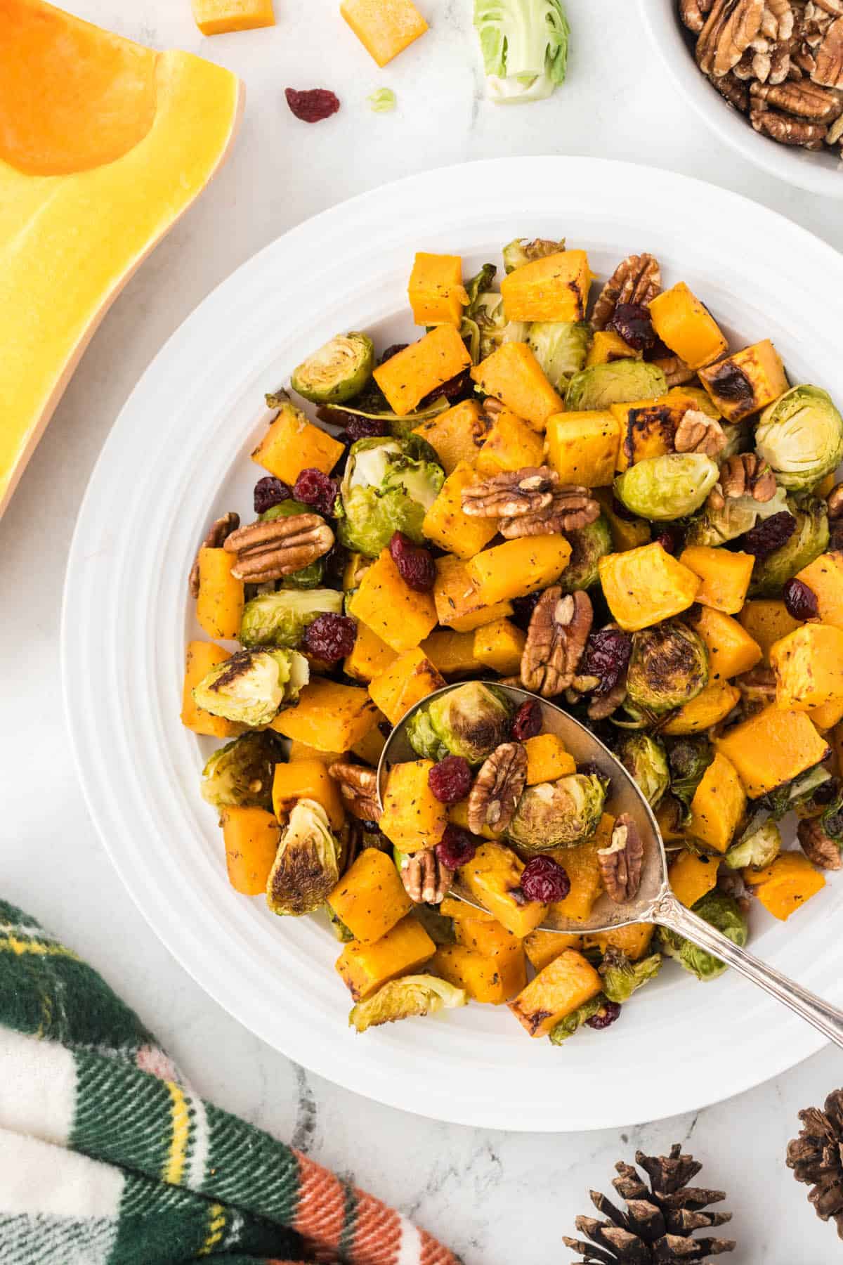 Roasted butternut squash and brussels sprouts in a serving bowl, with a serving spoon.