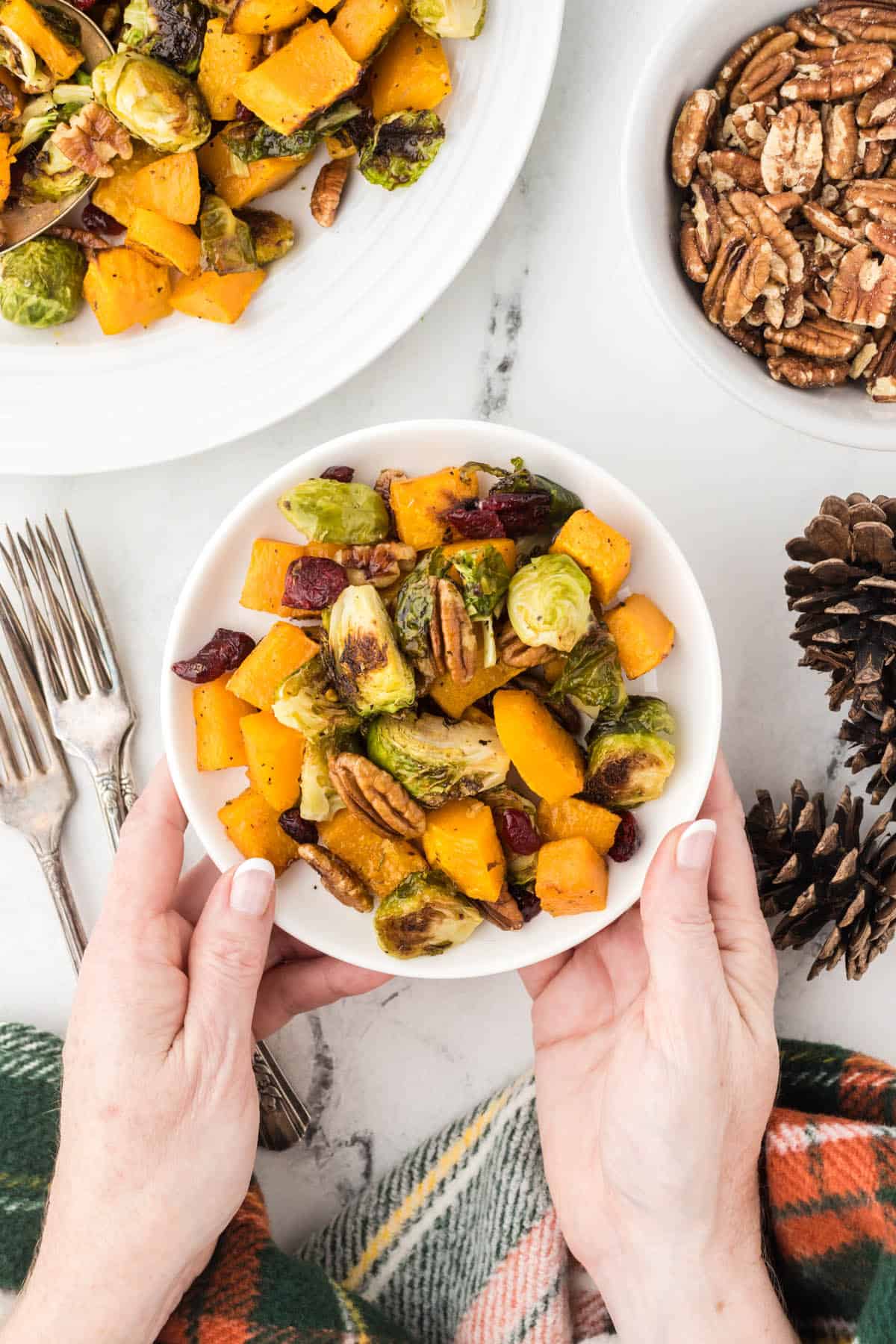 A hand holding a serving of roasted butternut squash and brussels sprouts in a bowl.