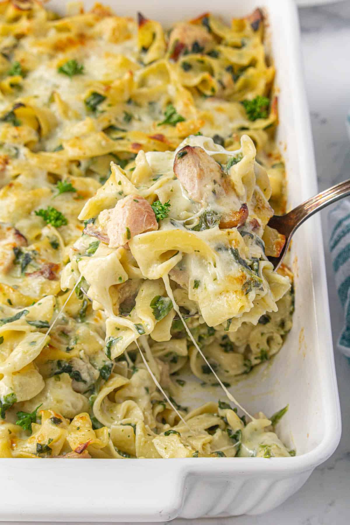 Smoked turkey pasta casserole in a baking dish with a big spoon scooping out a serving.