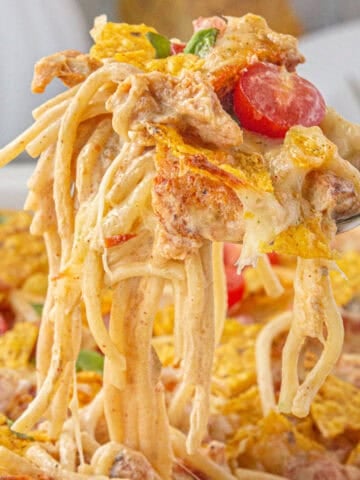 Gooey, cheesy queso chicken spaghetti in a dish. A serving is being scooped out.