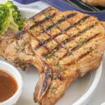 A grilled pork chop on a plate, ready to eat.