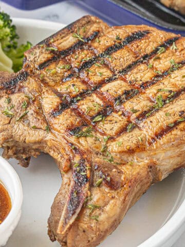 A grilled pork chop on a plate, ready to eat.