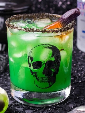 A green cocktail in a glass with a skull on it. This is a fun Halloween cocktail.