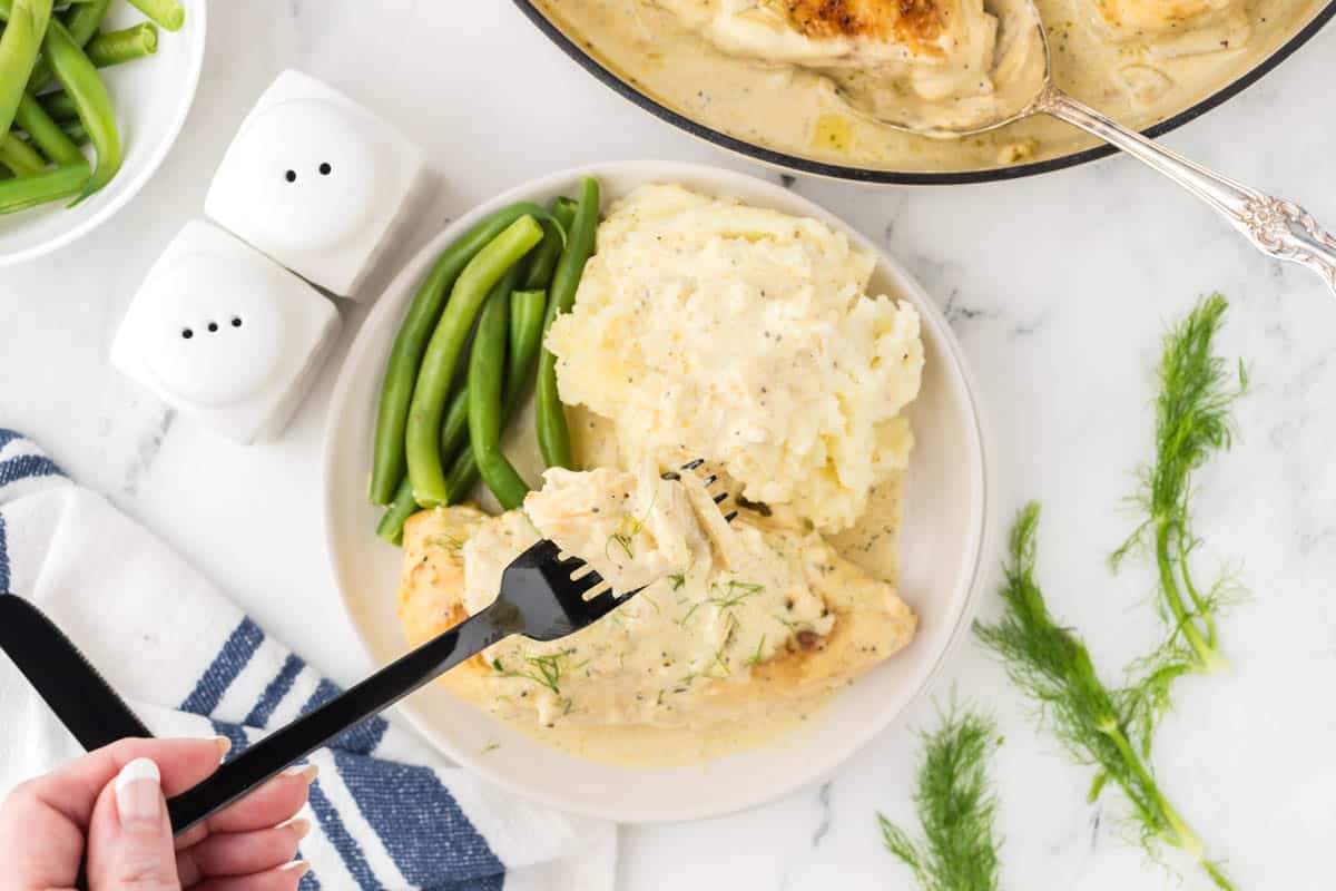 Baked chicken with white sauce on a plate with mashed potatoes and steamed green beans.