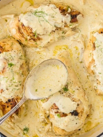 A cast iron skillet with baked chicken in gravy. With a serving spoon.