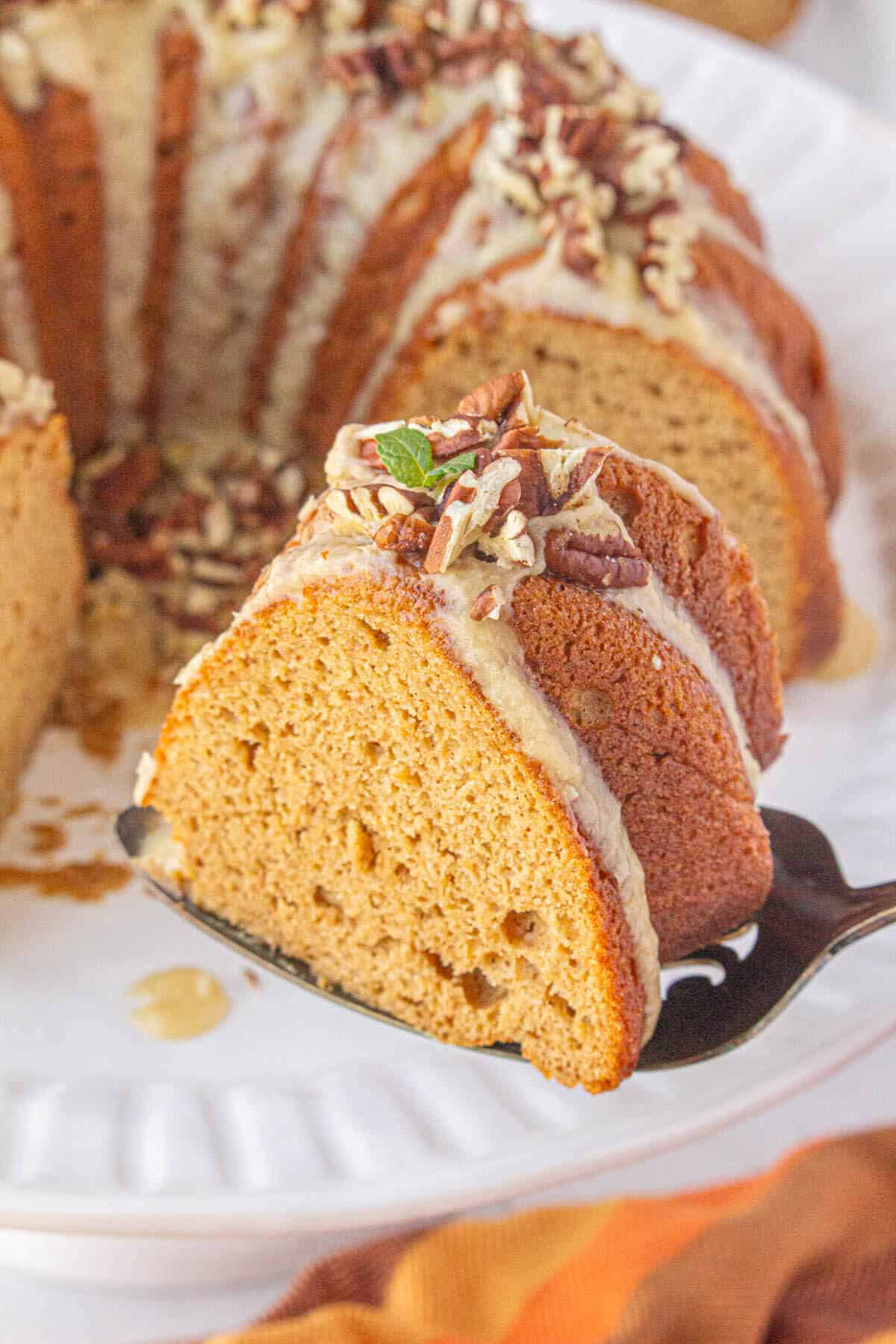 Sweet potato bundt cake on a cake stand, with a slice of cake on a spatula.