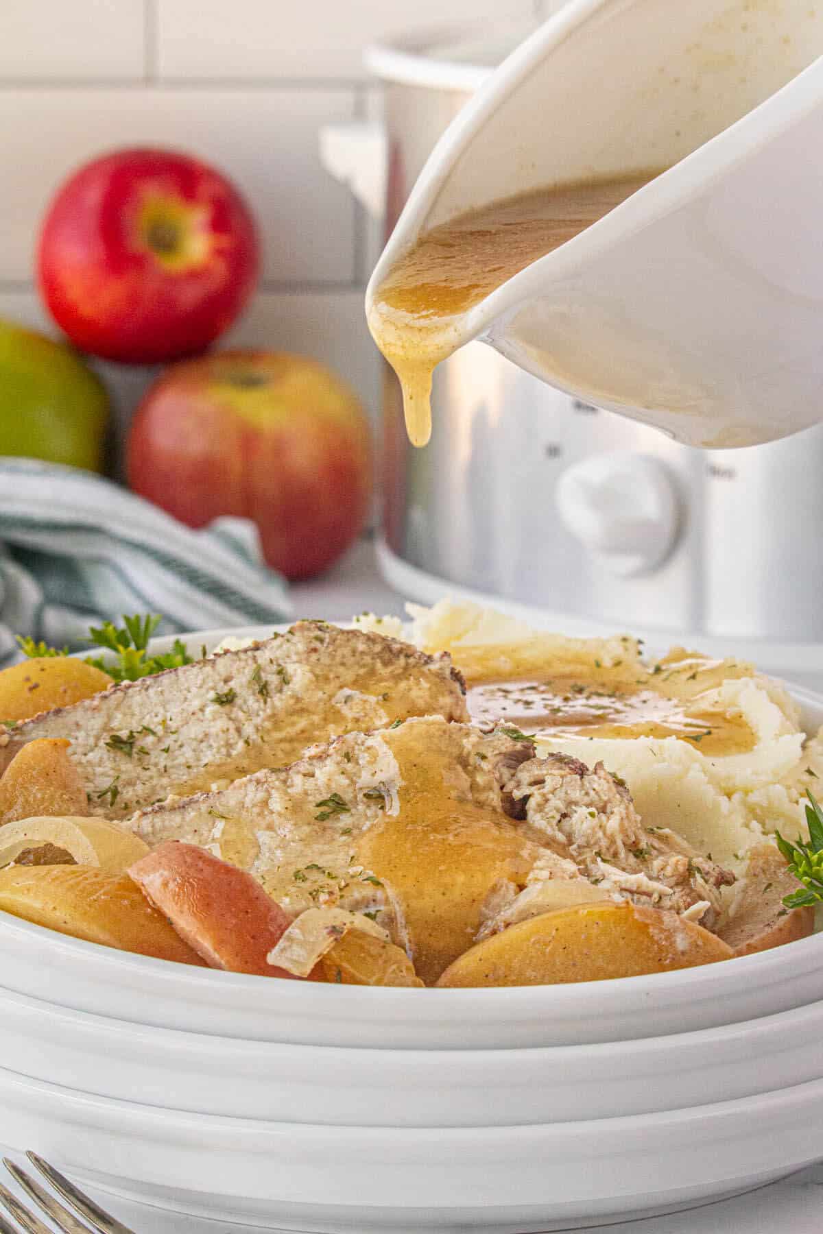 A plate filled with sliced roast pork with mashed potatoes. Gravy is being pork over the pork loin.