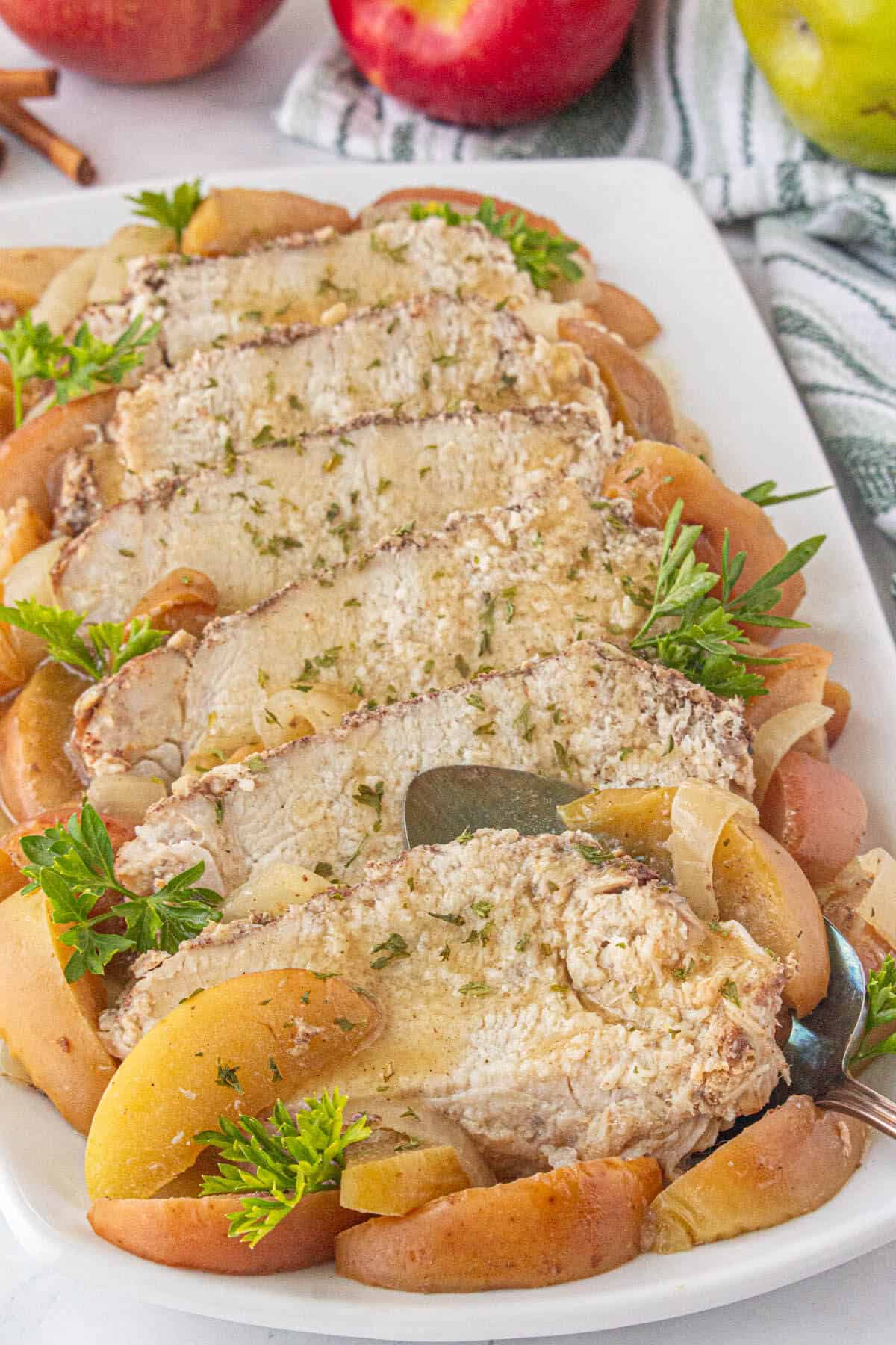 Sliced pork roast on a platter with a serving spatula. It is garnished with cooked sliced apples and onions.