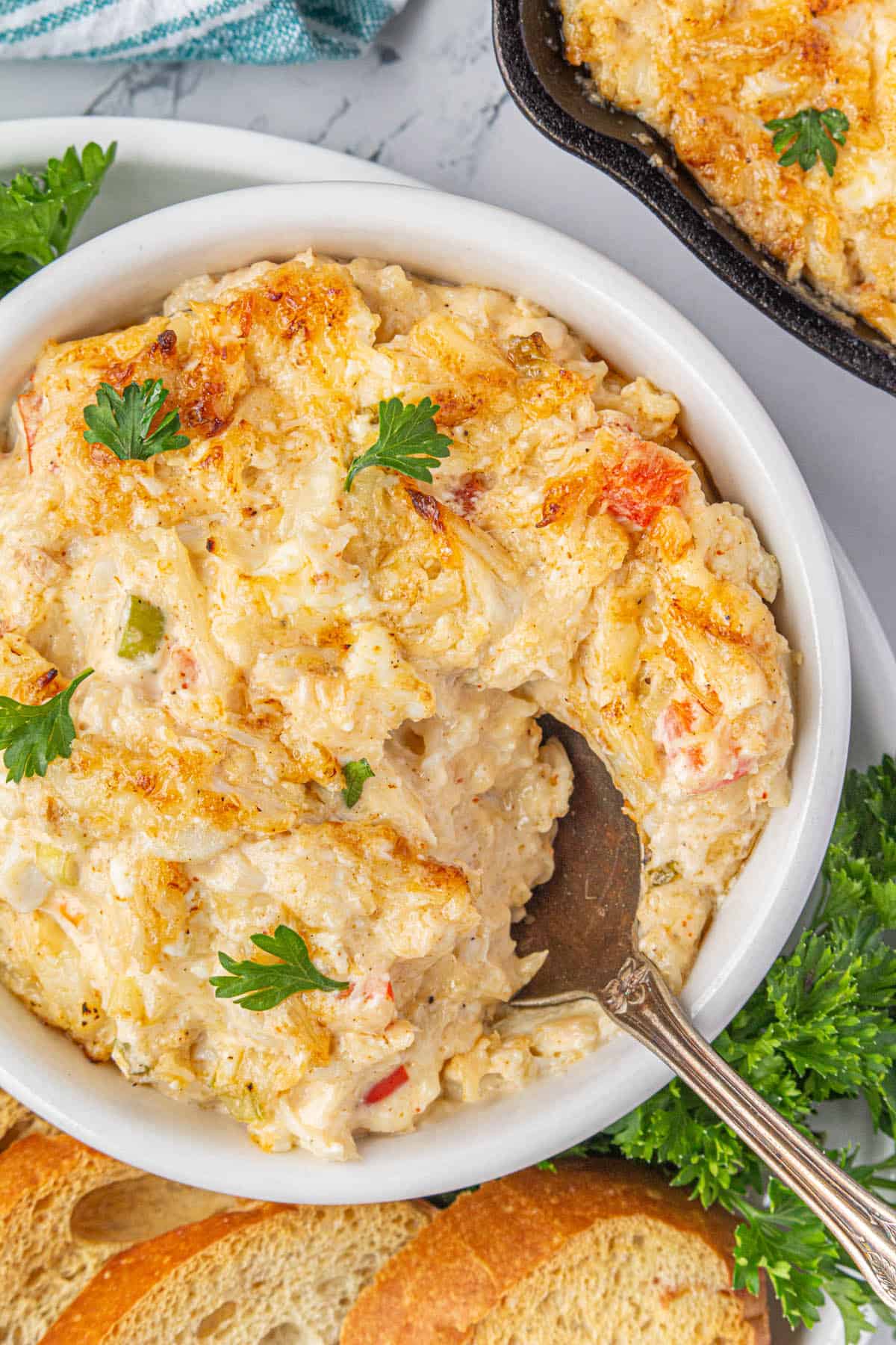 A white bowl filled with hot crab dip surrounded by toasted baguettes.