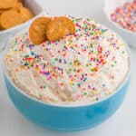 Funfetti Dip piled high into a blue bowl with vanilla wafers pushed into the dip.