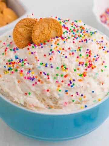 Funfetti Dip piled high into a blue bowl with vanilla wafers pushed into the dip.